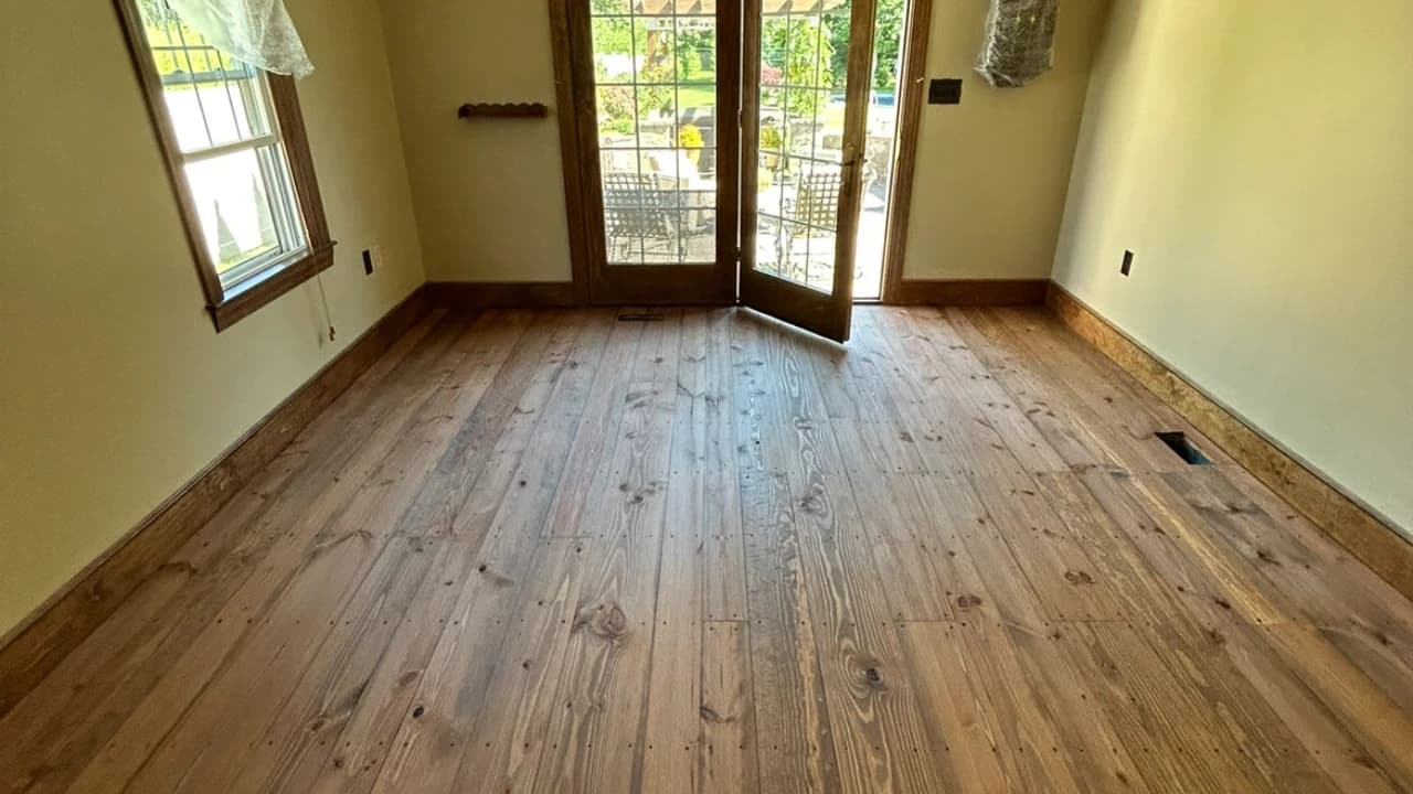 Refinished wide-plank pine floor in a sunlit room with French doors